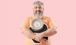 Overweight happy mature man with scales on pink background. Weight loss with tirzepatide.
