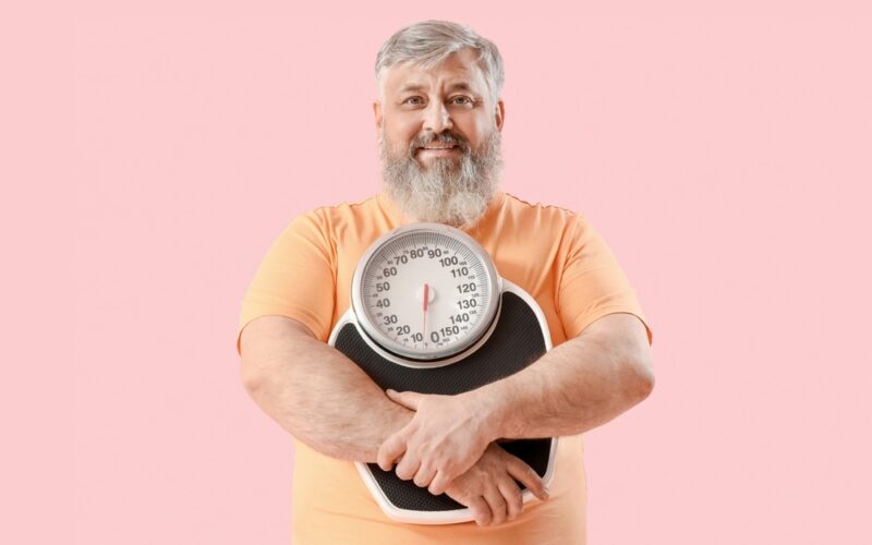 Overweight happy mature man with scales on pink background. Weight loss with tirzepatide.
