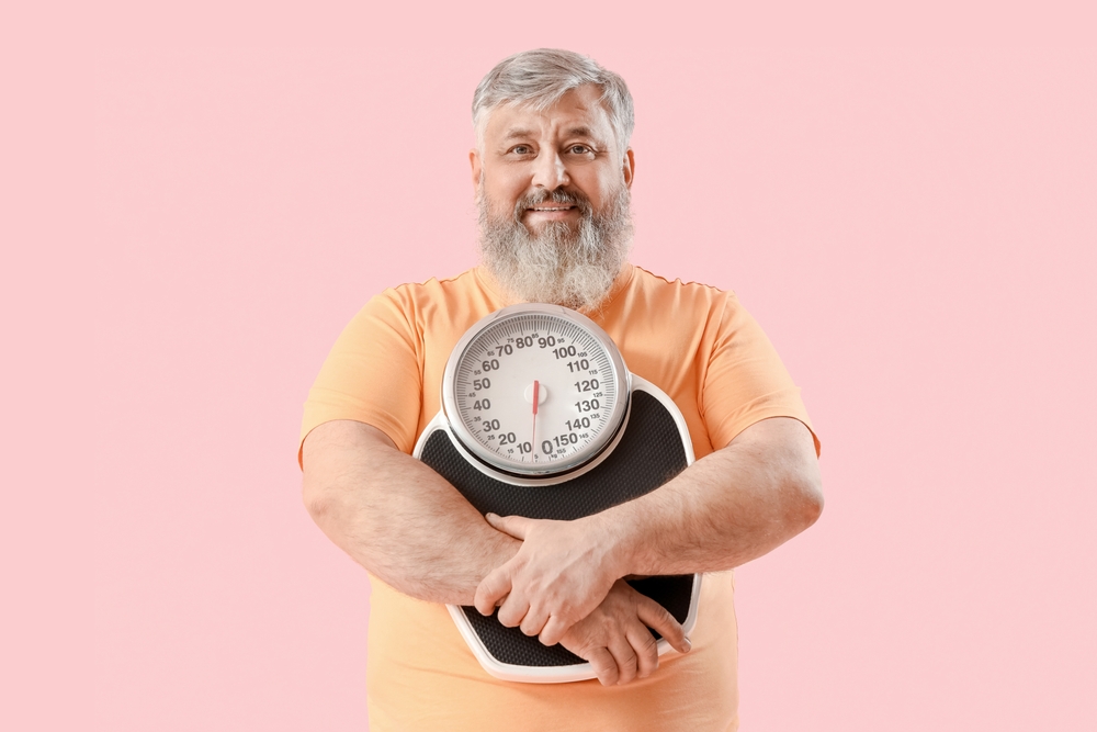 Overweight happy mature man with scales on pink background. Weight loss with tirzepatide.