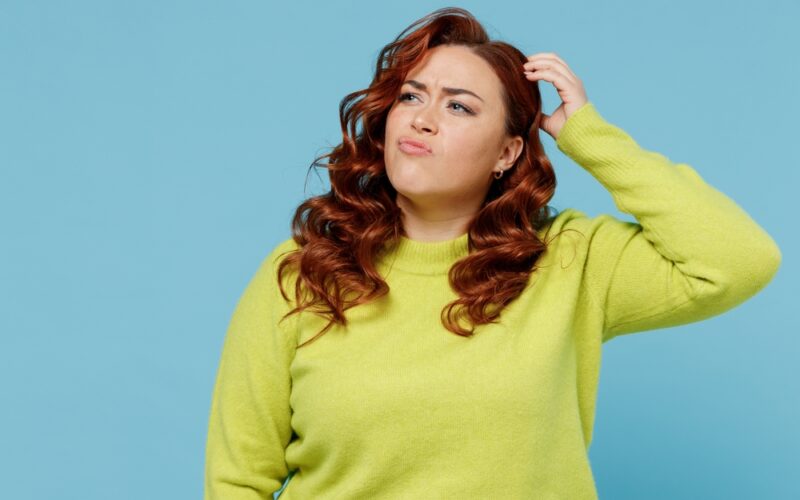 Young puzzled thoughtful confused chubby overweight plus size big fat fit woman wear green sweater look aside scratch head isolated on plain blue background studio portrait. People lifestyle concept Tirzepatide