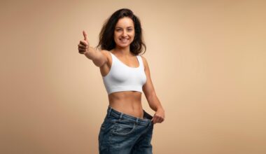 Smiling woman in a white sports bra giving a thumbs-up while holding out the waistband of her loose jeans, symbolizing successful weight loss with Zepbound (tirzepatide).
