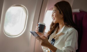 Woman traveling with tirzepatide, holding a coffee cup and phone while sitting on an airplane.