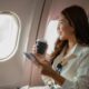 Woman traveling with tirzepatide, holding a coffee cup and phone while sitting on an airplane.