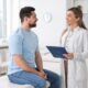 Male patient talking with a female doctor holding a clipboard during a consultation, representing medical guidance on vitamin B12 injections and their role in weight management.