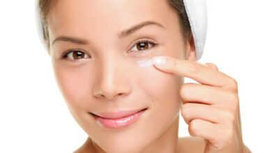 Close-up of a smiling woman applying cream under her eye with her fingertip, representing skincare and the cautious use of tretinoin in the delicate under-eye area.