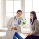 Female doctor sitting beside a smiling woman in a bright medical office, reviewing health information on a clipboard — representing patient guidance on managing acarbose side effects and improving comfort during diabetes treatment.
