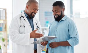 Smiling doctor discusses a treatment plan with a patient while reviewing a medical chart together in a bright clinic — representing supportive healthcare guidance and transparent discussion about medication costs.