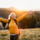 A joyful woman stands outdoors at sunset with her arms outstretched, wearing a yellow jacket and backpack, symbolizing energy, vitality, and rejuvenation — themes linked to the restorative benefits of NAD+ IV therapy and vitamin infusions.