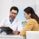 Smiling male doctor showing medical information on a clipboard to a female patient during a consultation, representing professional guidance on oral semaglutide (Rybelsus) dosing and safe weight management.
