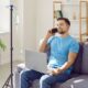 A relaxed, happy man sitting on a couch at home with an IV drip stand beside him, talking on the phone and using a laptop while receiving IV therapy.