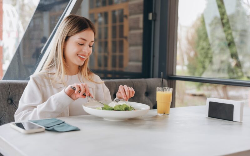A happy woman enjoying a healthy salad and juice, representing mindful eating and making smart dietary choices while managing weight and balancing alcohol intake.