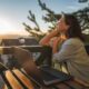 A happy woman sitting outdoors at a table with her laptop open, enjoying the fresh morning air while tracking her weight loss progress and lifestyle changes on Mounjaro (tirzepatide).