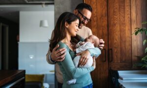 A happy couple stands together in their home, lovingly holding their newborn baby, symbolizing the natural bond, emotional connection, and well-being associated with oxytocin.