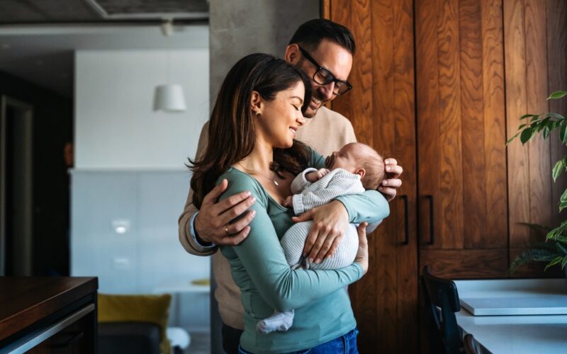 A happy couple stands together in their home, lovingly holding their newborn baby, symbolizing the natural bond, emotional connection, and well-being associated with oxytocin.