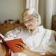 A woman sitting comfortably in a cozy, sunlit room writes in a red journal, appearing calm and reflective — symbolizing goal setting, self-awareness, and mindful tracking during her GLP-1 weight loss journey.