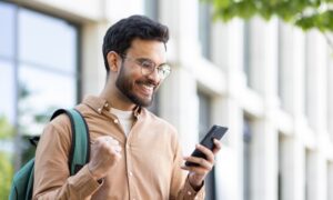 A smiling man outdoors looks excited while checking his phone, celebrating good news — representing successfully accessing a Zepbound discount or savings card.