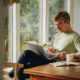 A man sits at a wooden table by a bright window, focused on his laptop with a notebook, coffee, and phone nearby—representing researching semaglutide prescriptions and taking proactive steps for weight management.