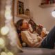 A woman relaxes on a cozy couch in a warmly lit living room, smiling as her cat gently touches noses with her — capturing the emotional comfort, bonding, and companionship central to life with an emotional support animal.
