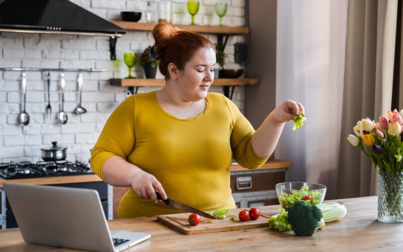 Woman preparing a healthy salad in a home kitchen, illustrating mindful eating, nutrition tracking, and strategies to overcome a weight loss plateau.