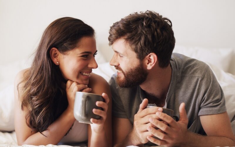 Smiling couple lying together in bed, representing intimacy and sexual health topics related to zepbound, weight loss, and sex drive changes.