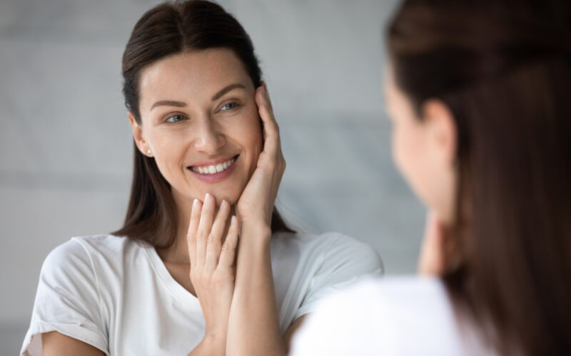 Woman examining her skin in a mirror, representing interest in collagen peptides and skin health benefits