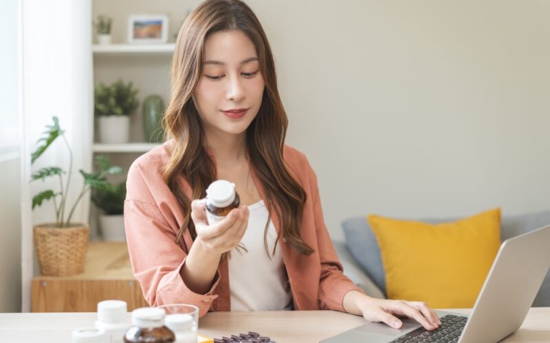 A woman at home reviewing medication bottles while using a laptop, representing research into Wegovy alternatives and weight-loss treatment options