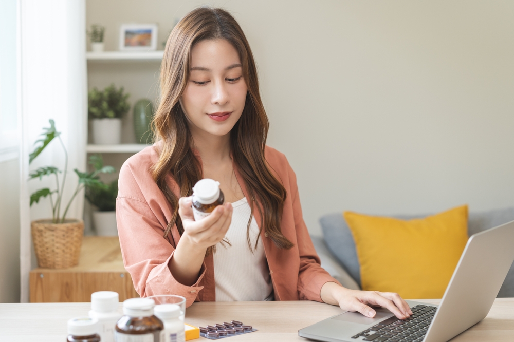 A woman at home reviewing medication bottles while using a laptop, representing research into Wegovy alternatives and weight-loss treatment options