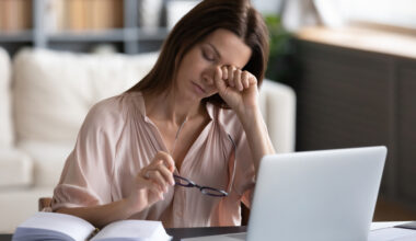 Tired woman sitting at a computer, resting her head on her hand, looking fatigued and overwhelmed, representing chronic fatigue syndrome and the potential role of B12 injections.