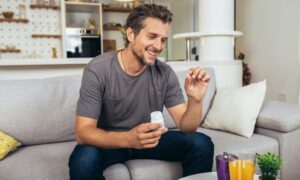 Man at home holding an erectile dysfunction pill and medication bottle, illustrating how ED pills like Viagra and Cialis work to support erections through improved blood flow.