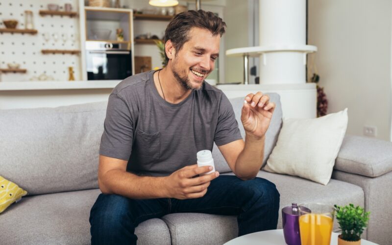 Man at home holding an erectile dysfunction pill and medication bottle, illustrating how ED pills like Viagra and Cialis work to support erections through improved blood flow.