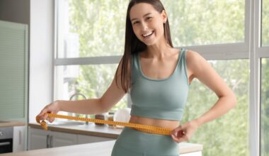 Smiling woman measuring her waist with a tape measure at home, representing hormone-driven weight loss, improved metabolism, and progress with GLP-1 medications.
