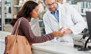 Pharmacist counseling a woman at a pharmacy counter, representing discussions about access to investigational weight loss medications like retatrutide before FDA approval.
