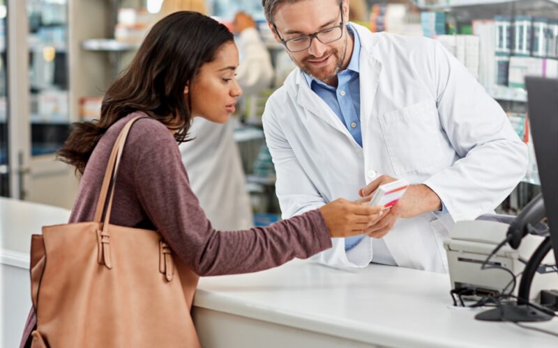 Pharmacist counseling a woman at a pharmacy counter, representing discussions about access to investigational weight loss medications like retatrutide before FDA approval.