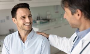 Doctor speaking reassuringly with a male patient in a medical office, representing a supportive conversation about erectile dysfunction diagnosis and treatment options