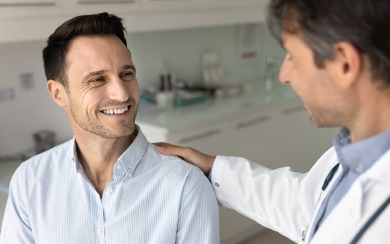 Doctor speaking reassuringly with a male patient in a medical office, representing a supportive conversation about erectile dysfunction diagnosis and treatment options