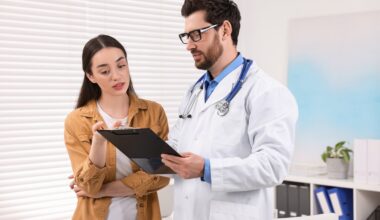 A doctor holding a clipboard explains a medication dosing plan to a woman in a clinical office, both reviewing information together.