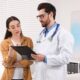 A doctor holding a clipboard explains a medication dosing plan to a woman in a clinical office, both reviewing information together.
