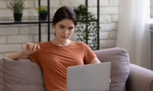Woman sitting on a couch using a laptop, researching out-of-pocket costs and affordable options for semaglutide without insurance.