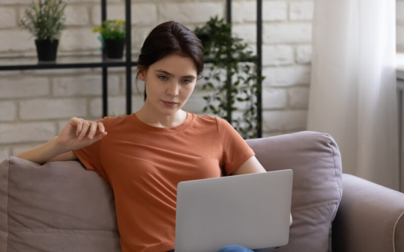 Woman sitting on a couch using a laptop, researching out-of-pocket costs and affordable options for semaglutide without insurance.