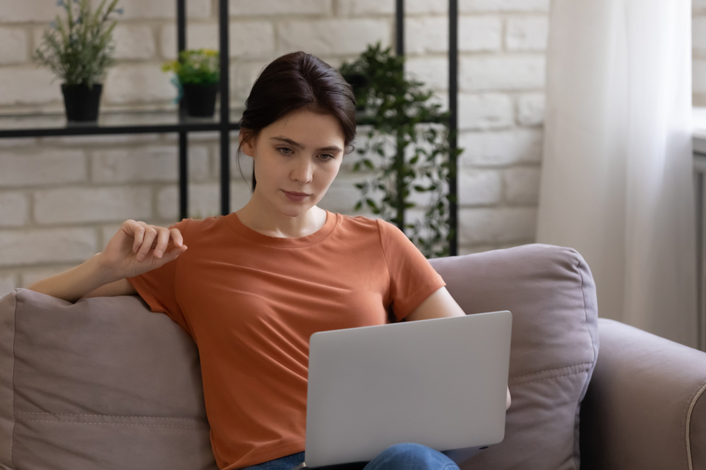 Woman sitting on a couch using a laptop, researching out-of-pocket costs and affordable options for semaglutide without insurance.