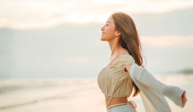 Woman smiling with arms outstretched on the beach at sunset, reflecting increased confidence and wellbeing associated with the semaglutide glow-up.