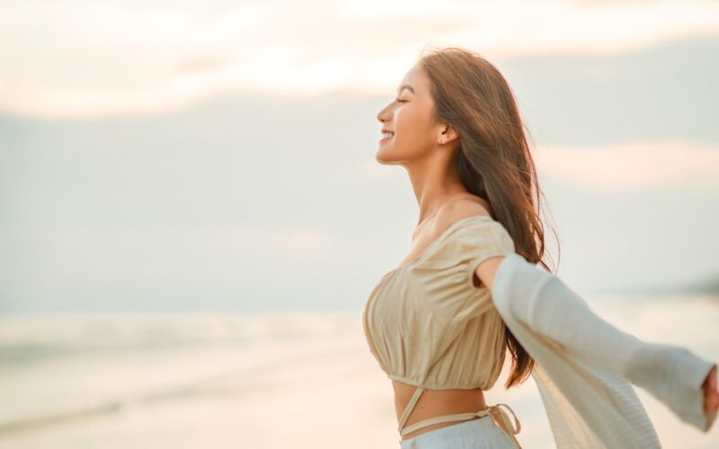 Woman smiling with arms outstretched on the beach at sunset, reflecting increased confidence and wellbeing associated with the semaglutide glow-up.