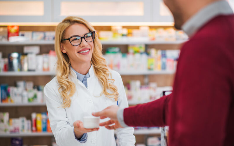 Pharmacist handing a medication container to a customer, representing questions about compounded semaglutide safety, legality, and pharmacy dispensing.