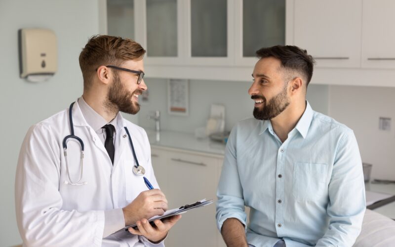 A doctor talking with a male patient during a first weight loss lab visit, discussing symptoms and lab testing.