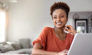 Woman smiling while using a laptop at home, learning about Mounjaro dosing schedule and tirzepatide titration for weight loss and diabetes management.
