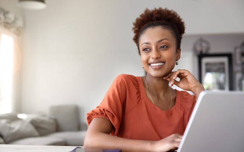 Woman smiling while using a laptop at home, learning about Mounjaro dosing schedule and tirzepatide titration for weight loss and diabetes management.