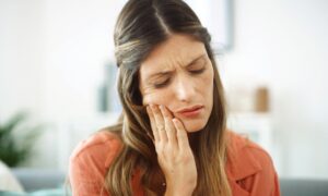 Woman feeling her mouth for tooth pain, possibly caused by ozempic teeth decay.