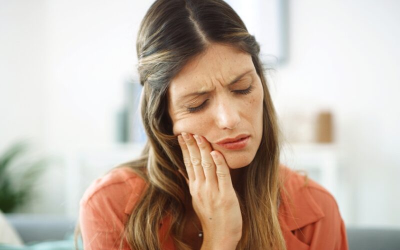 Woman feeling her mouth for tooth pain, possibly caused by ozempic teeth decay.