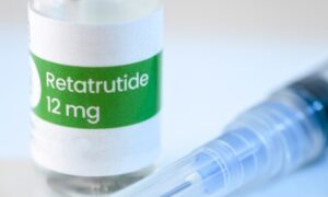 A vial of Retatrutide triple agonist injection sitting on a sterile white surface next to a medical syringe.